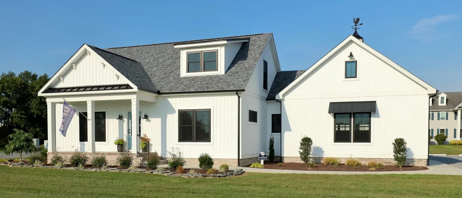 A finished white Beracah farmhouse with a standing-seam porch roof, seen across a clipped lawn.