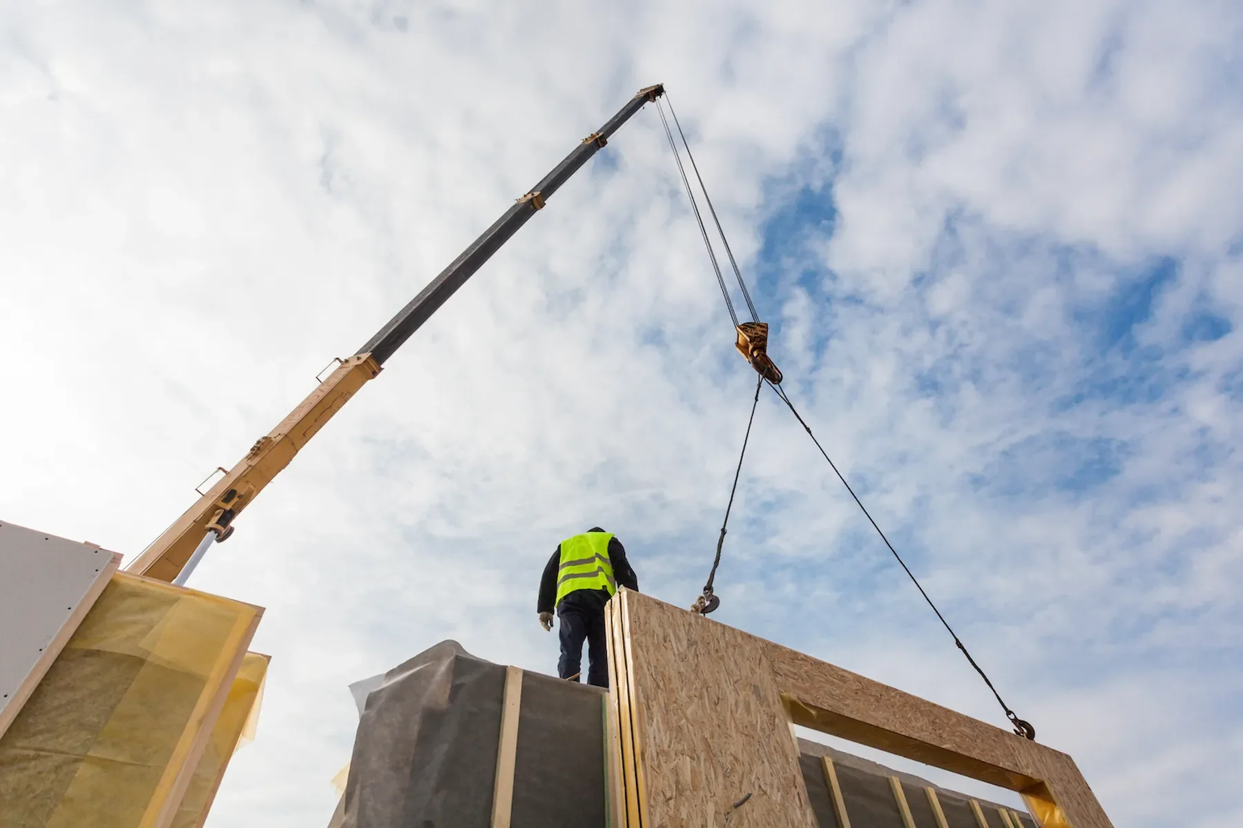 A crane lifting a Beracah module off its carrier while a crew member in a safety vest guides it from above.
